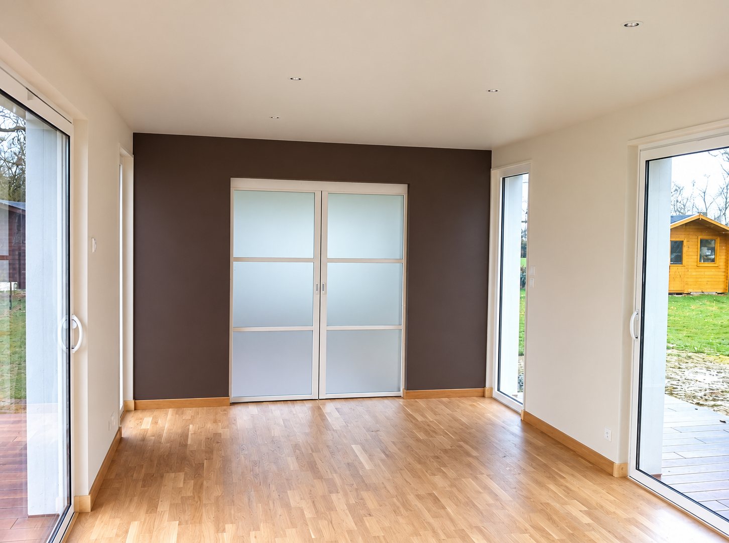 Pièce lumineuse récemment rénovée avec parquet clair, mur taupe, double porte coulissante en verre dépoli et grandes baies vitrées donnant sur le jardin.